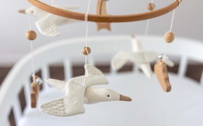 Houten babymobiel met zachte vogeltjes en houten kraaltjes boven een wit babybedje, als onderdeel van een sfeervol ingerichte babykamer.
